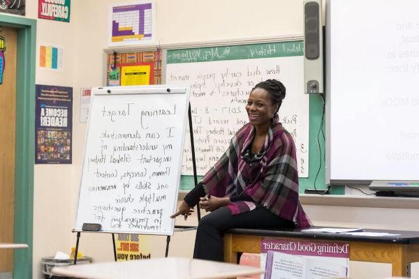 A teacher laughing at the front of a classroom, discussing learning targets with her students