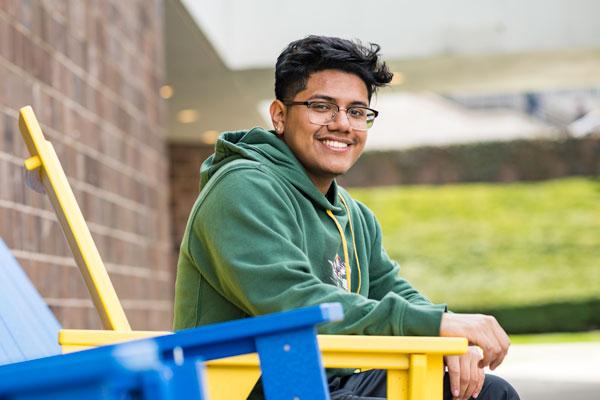 University of Rochester Student, Justin Pimentel ‘23, a computer science/history double major and first generation student from the Bronx, sitting on a yellow chair on campus.